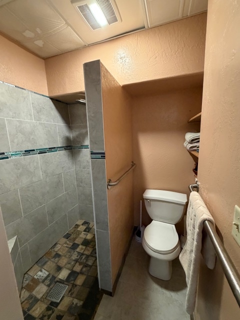 A compact bathroom featuring a walk-in shower with gray tiles and a multi-colored stone floor next to a white toilet.