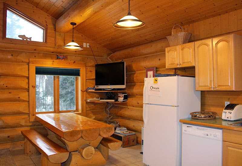 A cozy log cabin kitchen featuring a wooden dining table, refrigerator, and television.