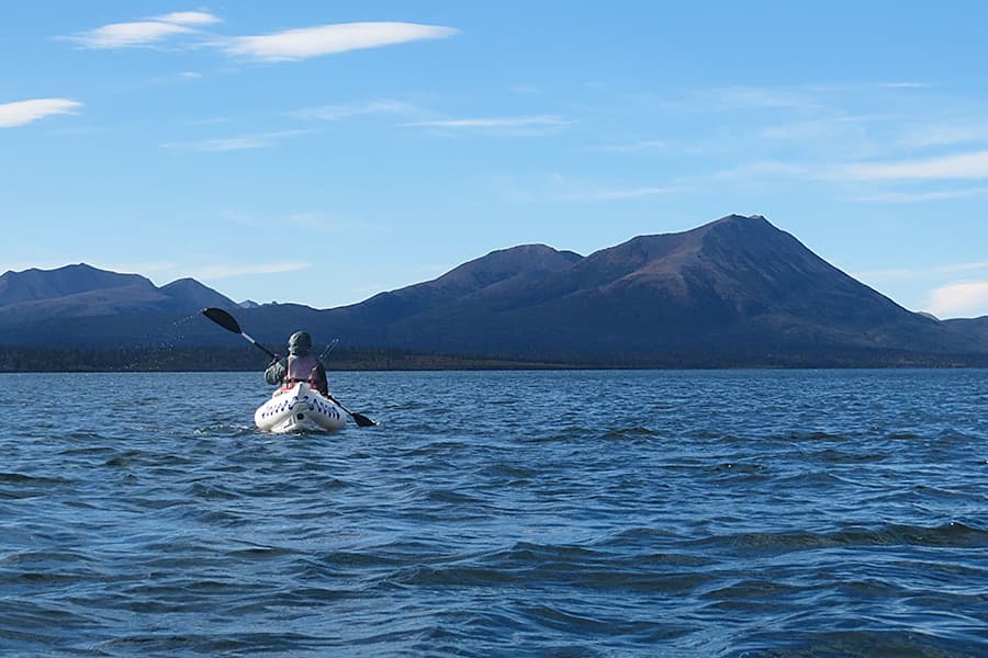 A person kayaking on a lake with mountains in the background.