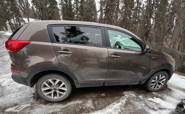 A brown SUV is parked on a snowy road surrounded by trees.